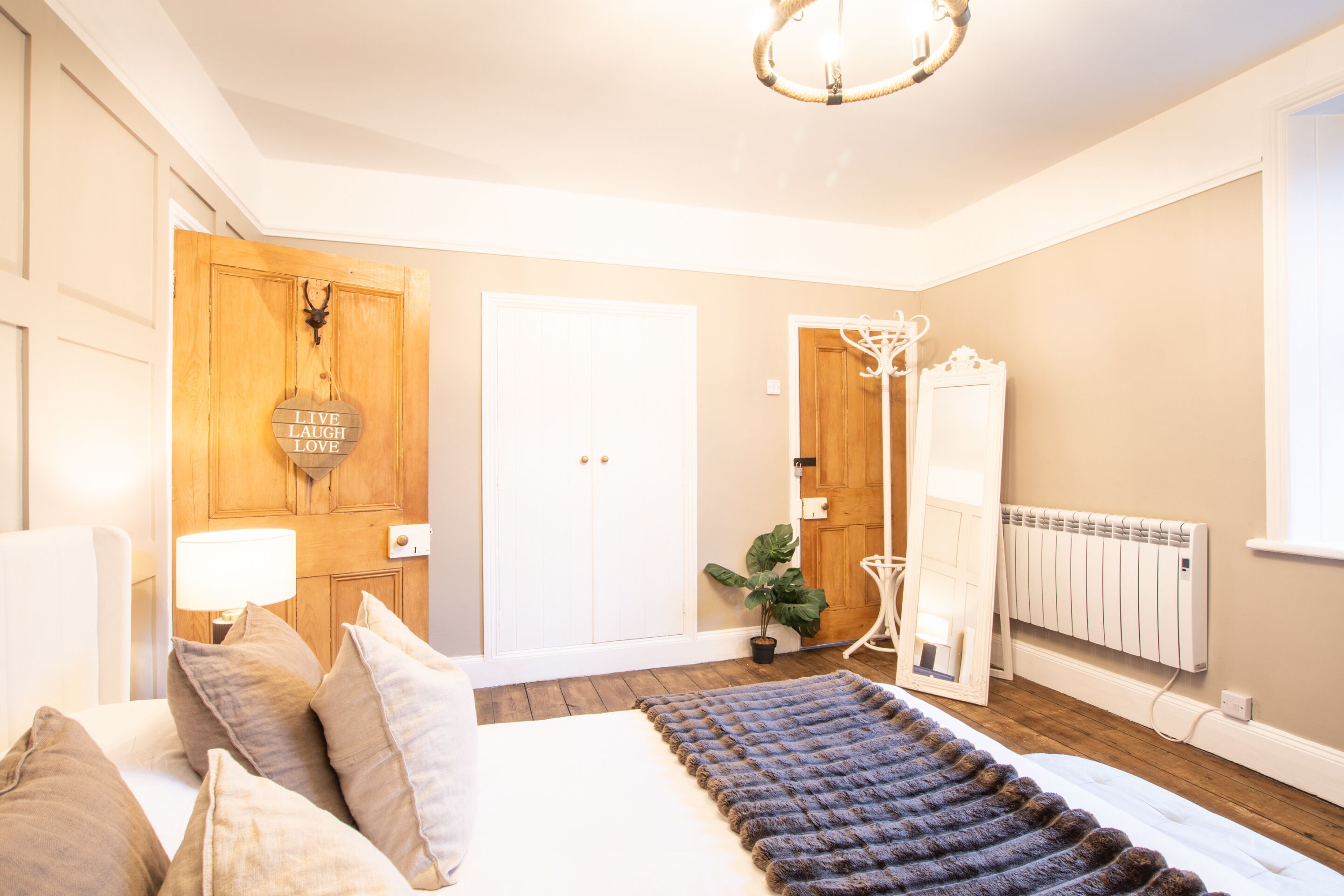 A bedroom with a bed, bedside lamps, a wooden wardrobe, a mirror, and a radiator.