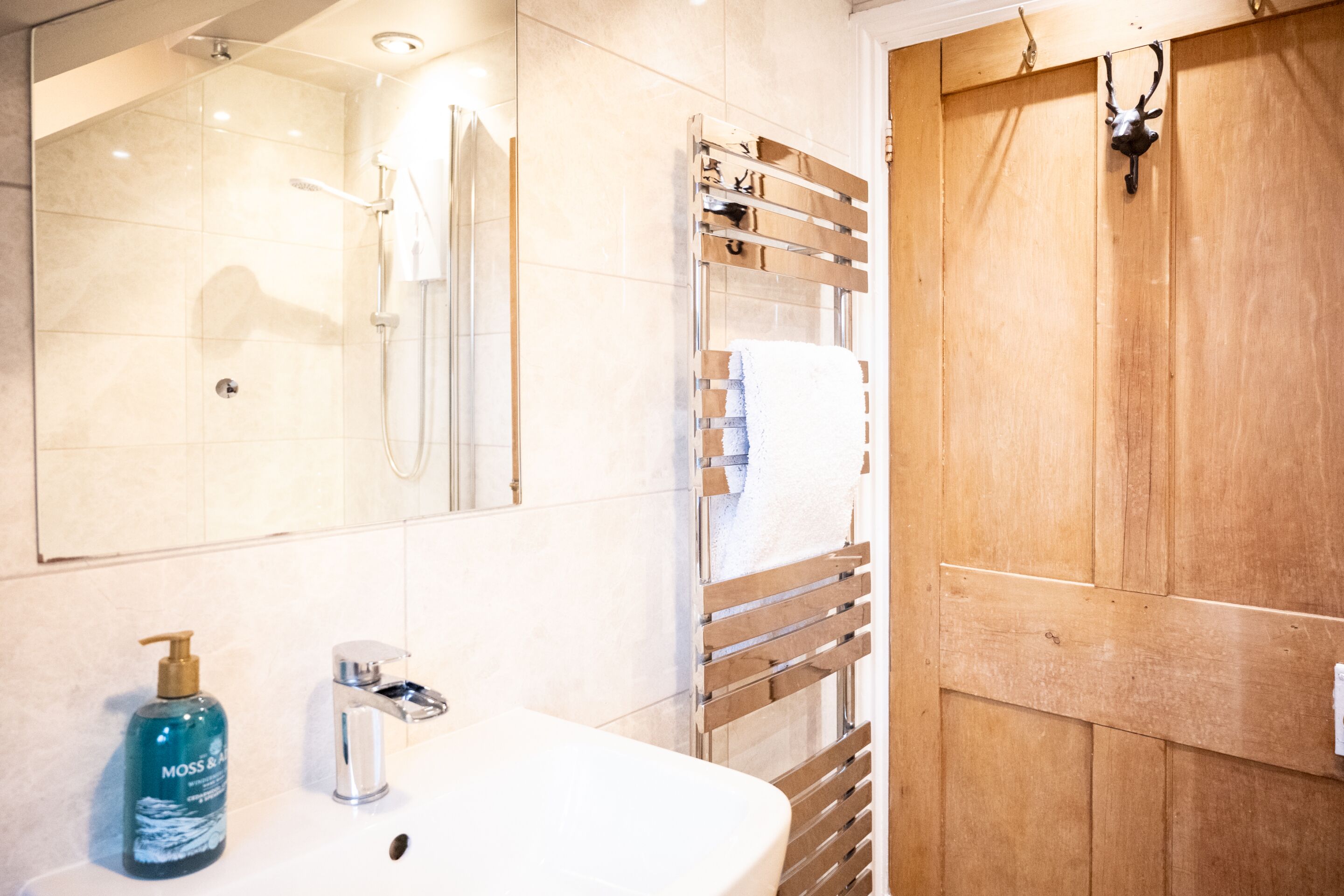 A bathroom with a white sink, a mirror, a shower, and a wooden door.