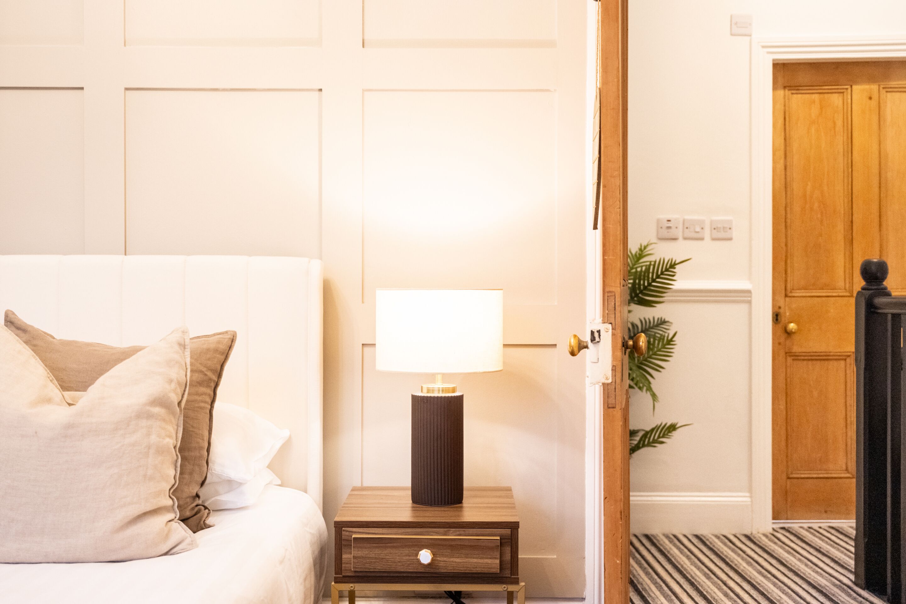 Et hotelværelse med en seng, et natbord med en lampe, en dør og en plante.