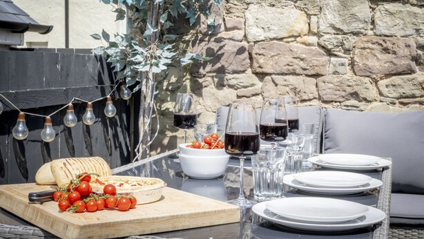 Un'area pranzo all'aperto con un muro in pietra, un tavolo di legno e una ghirlanda luminosa.