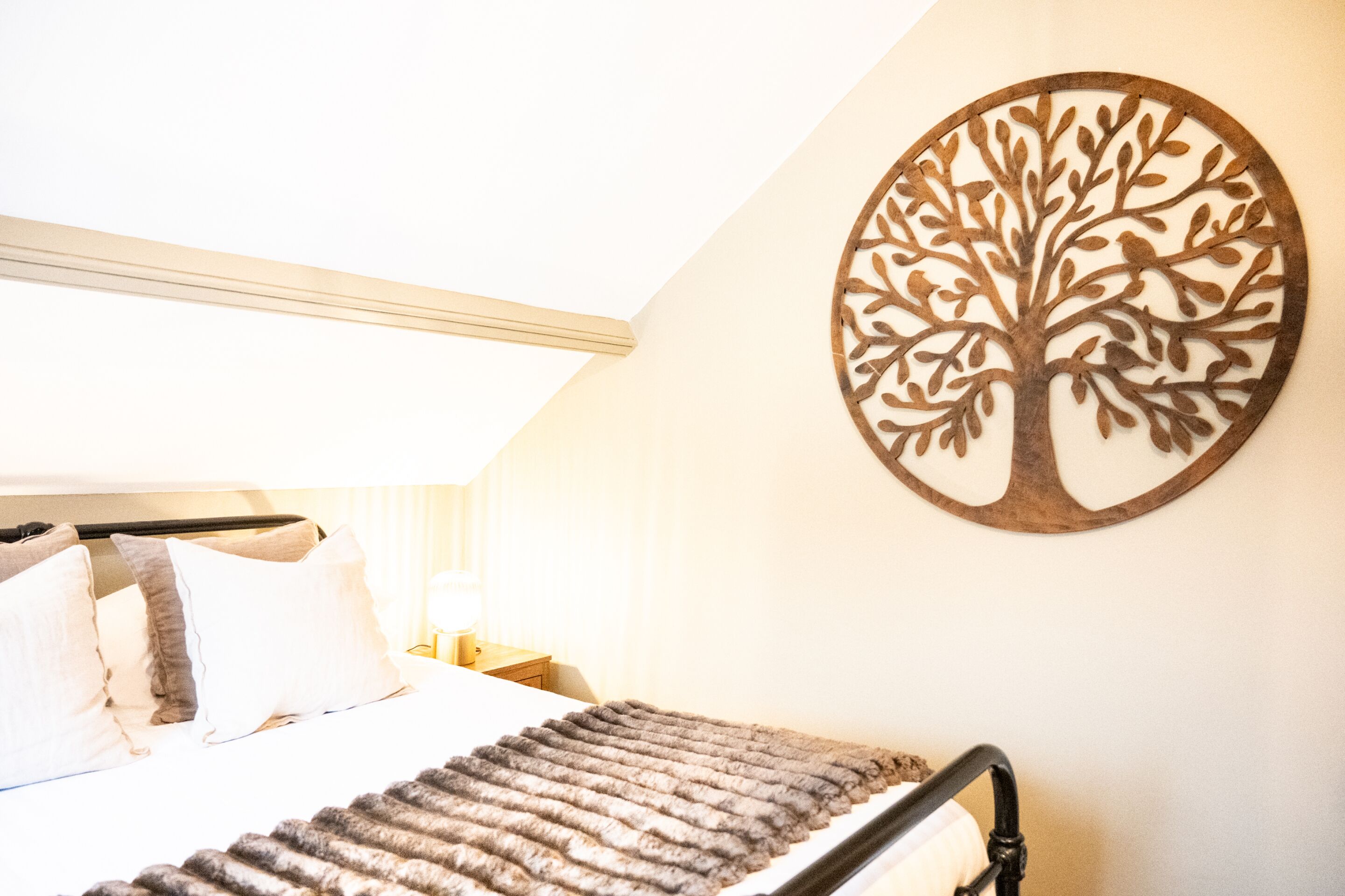 A bedroom with a bed, pillows, a blanket, and a wall-mounted tree decoration.