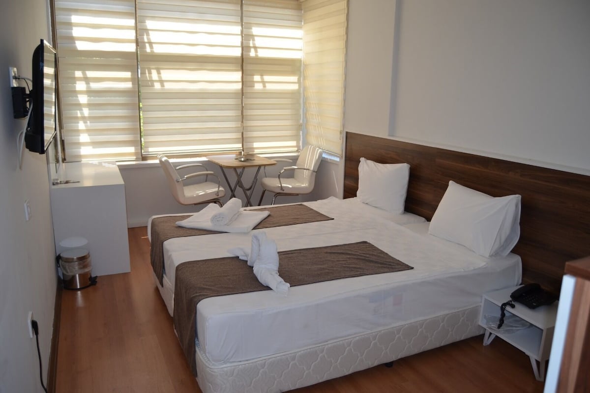 A hotel room with a large bed, a desk with a chair, a small table, and a TV mounted on the wall.