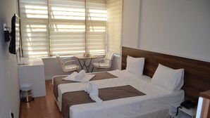 Quarto de hotel com uma cama grande, duas mesas de cabeceira, uma escrivaninha com cadeiras e uma janela com persianas.