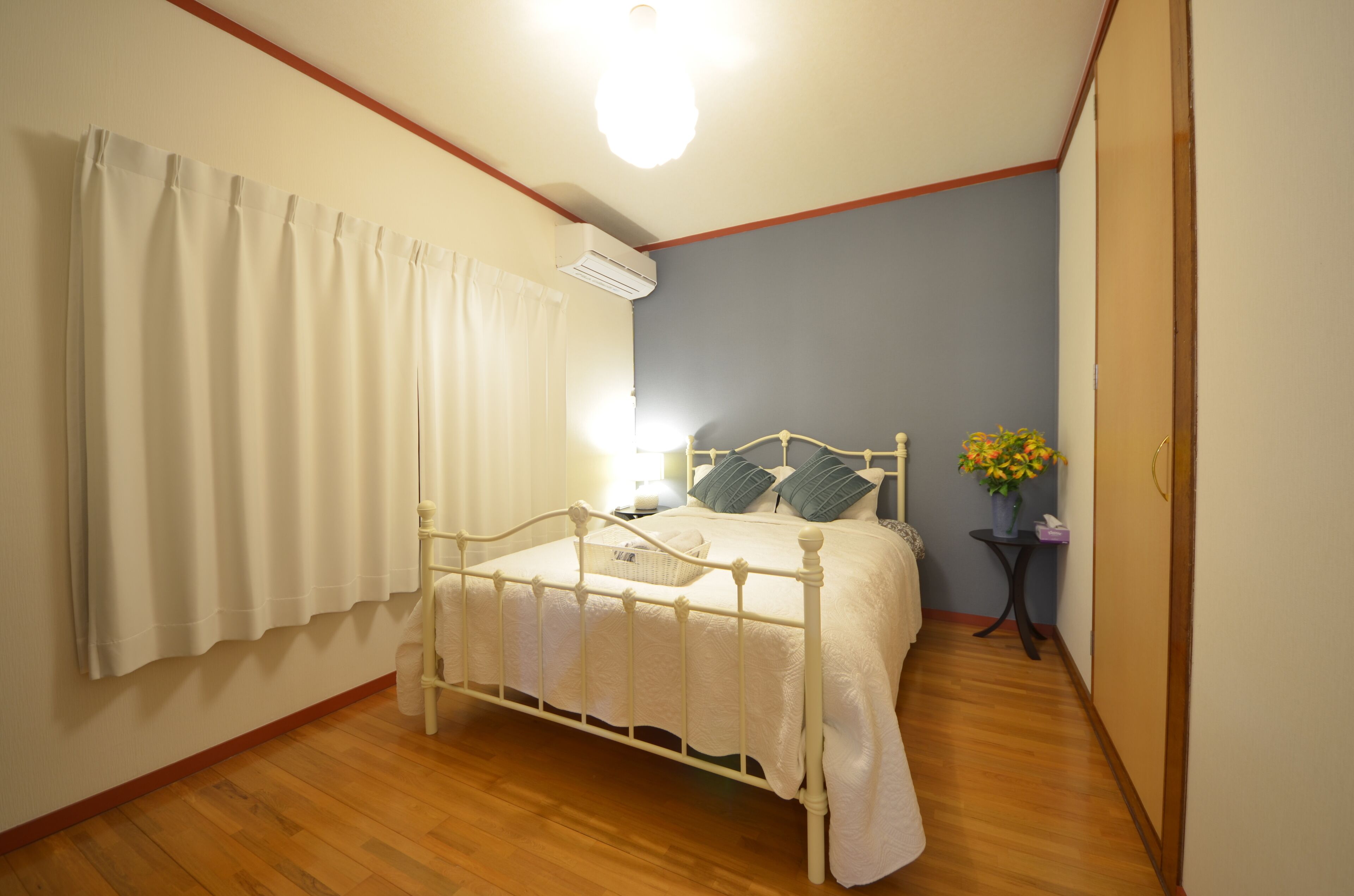 A bedroom with a bed, curtains, a bedside table with a lamp, and a small table with flowers.