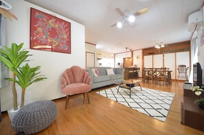 Een moderne woonkamer met een grijze bank, een roze fauteuil, een salontafel en een groot decoratief wandobject.