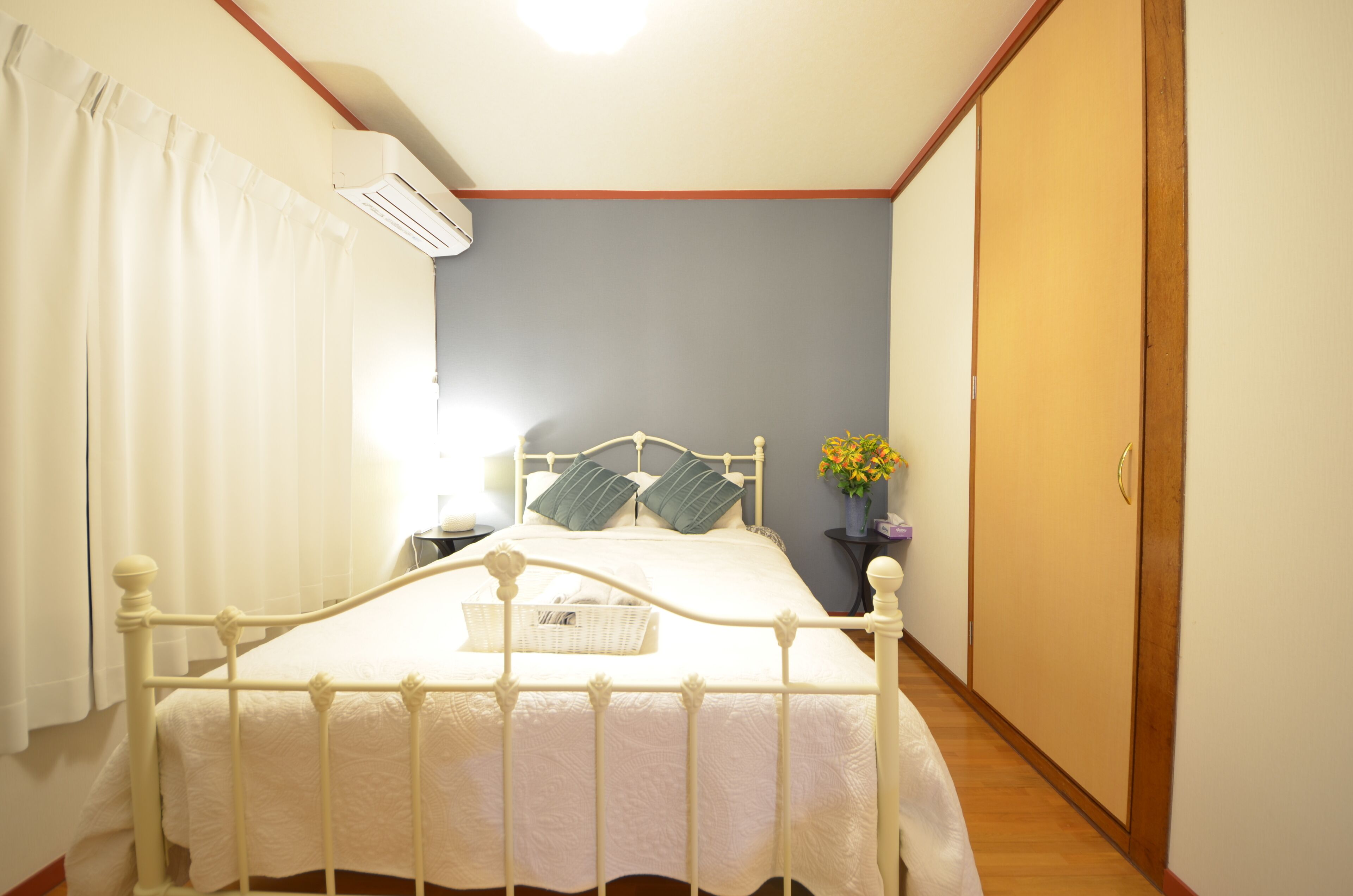 Een slaapkamer met een bed, nachtkastje, wandairconditioner, houten deur en gordijn.