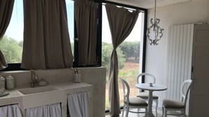 A room with a window, curtains, a sink, a table, chairs, and a chandelier. - Relais Grottone (Ostuni)