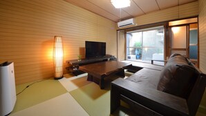 Ein Zimmer mit Tatami-Boden, einem Holztisch, einer Couch, einem Fernseher und einer Klimaanlage.