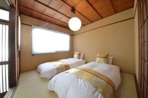 A traditional Japanese-style room with tatami flooring, two beds with matching bedding, a wooden ceiling, and a large window with blinds. - Kyoto Kosakacho House (Kyoto)