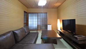 Ein Zimmer mit einer Couch, einem Fernseher auf einem Holzständer, einem kleinen Tisch und einer Schiebetür mit Gittermuster.