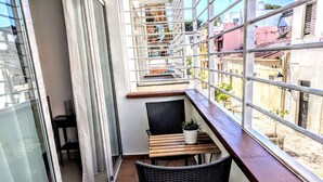 Ein Balkon mit einem Holztisch, einem schwarzen Korbstuhl und einem Blumentopf.
