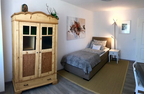 A bedroom with a bed, a nightstand, a wooden wardrobe, a painting, and a floor lamp.