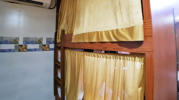 Une pièce avec une échelle en bois, une fenêtre ornée de rideaux jaunes et un appareil de climatisation fixé au mur.