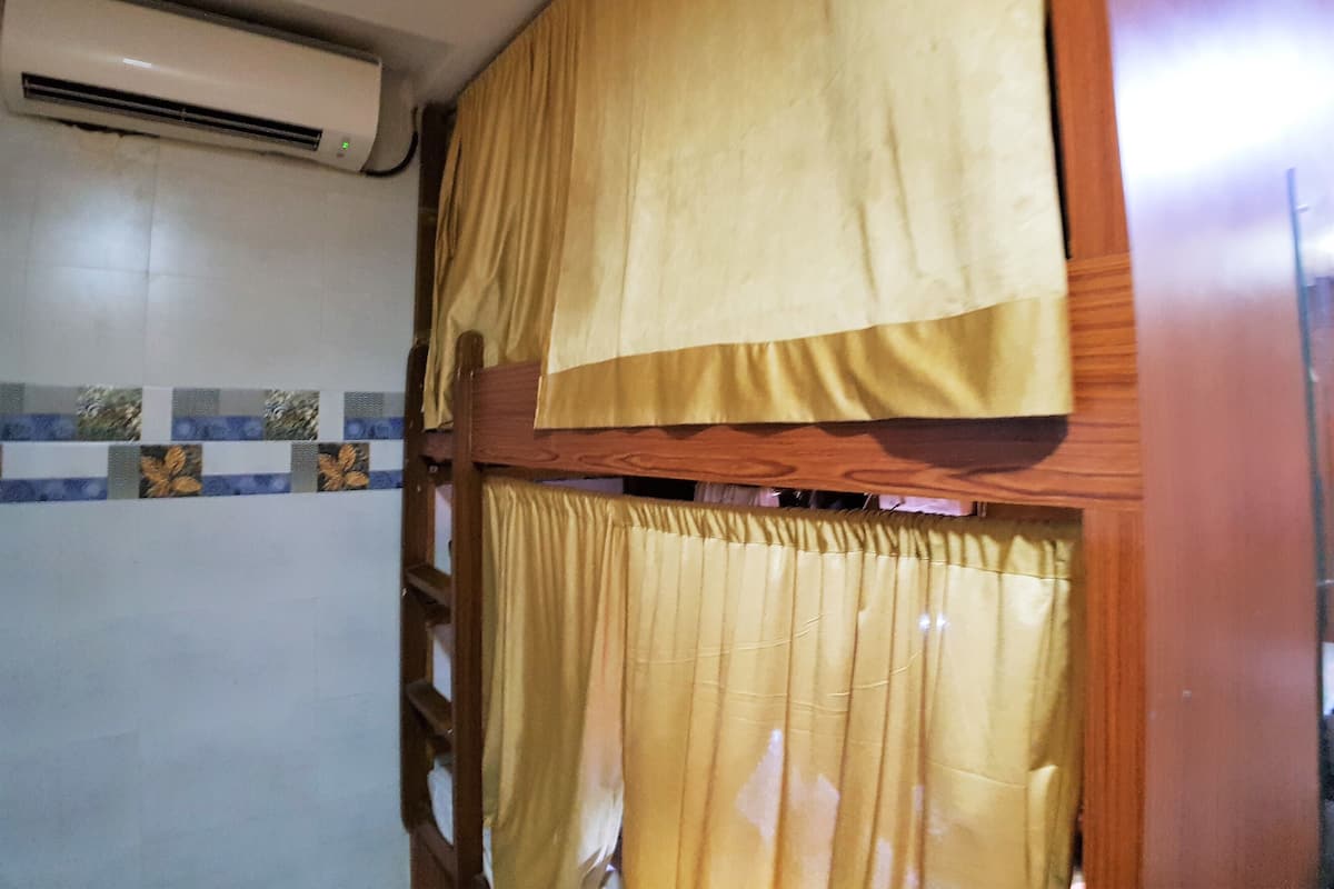 A room with a wooden ladder, a window with yellow curtains, and an air conditioning unit on the wall.