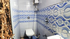 Une salle de bain comprenant des toilettes, un bidet et un lavabo. Les murs sont recouverts de carreaux aux motifs bleus et blancs.