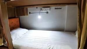 Un lit simple avec une tête de lit, une petite armoire et un luminaire placé au-dessus.