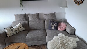 Una sala de estar moderna con un sofá seccional gris, cojines decorativos, una mesa de centro de madera y un otoman blanco y mullido.