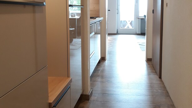 Un estrecho pasillo con suelo de madera que conduce a una zona de cocina.