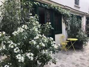 A courtyard with a yellow chair and table, surrounded by lush greenery and white flowering plants.