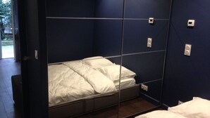 Quarto pequeno com uma cama, um espelho e uma porta.