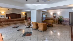 Un hall d’entrée spacieux avec un comptoir de réception, des fauteuils en osier, un grand miroir et une plante en pot.
