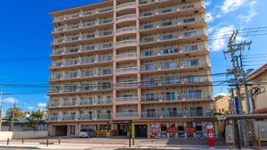 Un hôtel à plusieurs étages doté de balcons, un restaurant situé au rez-de-chaussée et un ciel d’un bleu limpide.