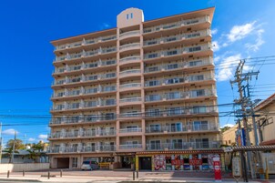 Un hotel de varios pisos con balcones, un restaurante a nivel de calle y un cielo azul despejado.