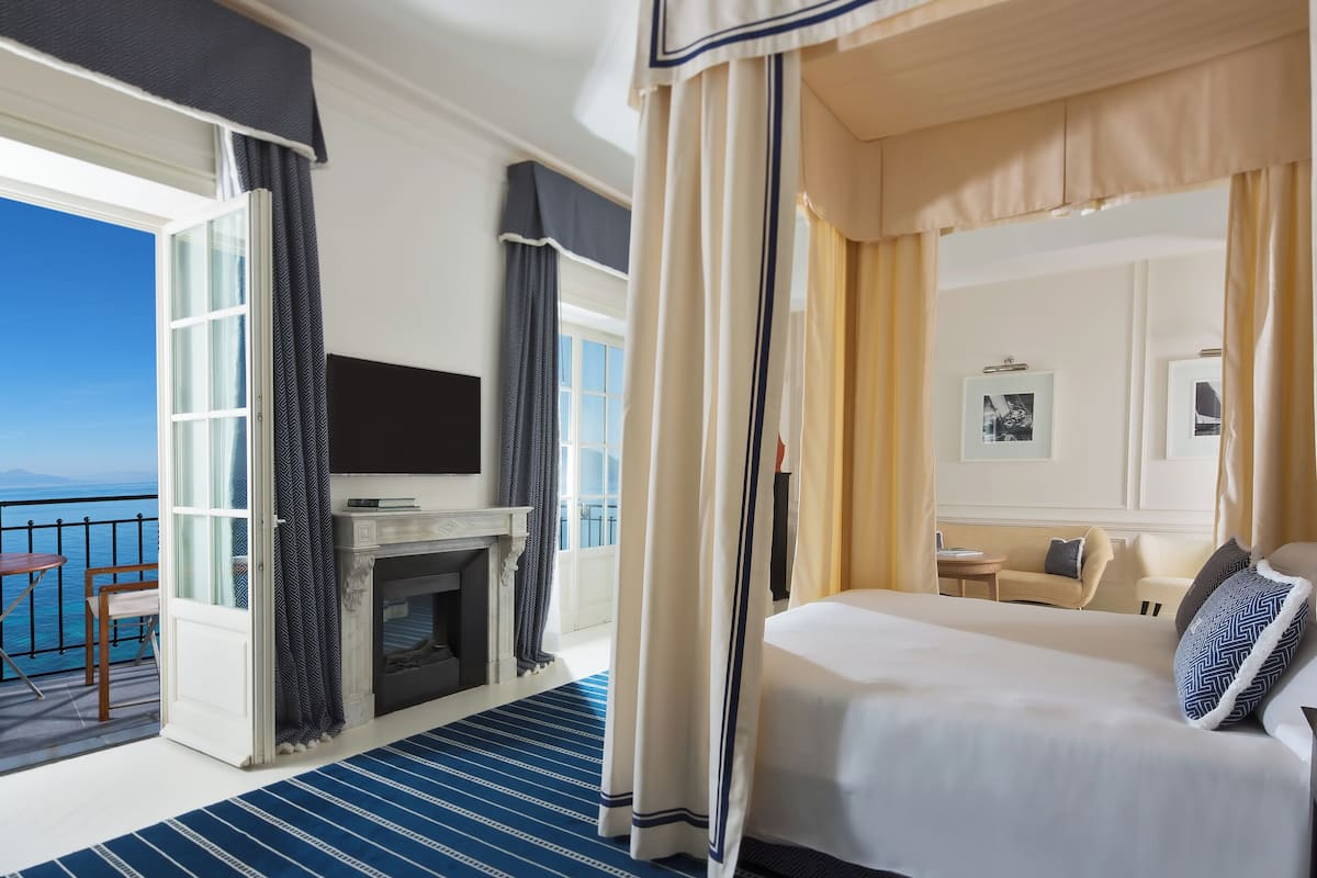A hotel room with a balcony, a fireplace, a bed, and a view of the sea.
