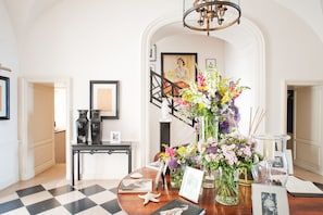 A well-lit room with a checkered floor, a wooden table with various items including a vase of flowers, framed pictures, and a starfish decoration.