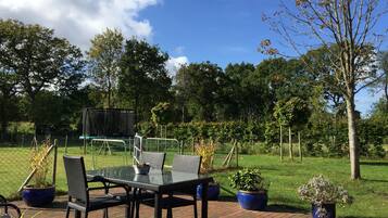 Eine Terrasse im Freien mit Tisch und Stühlen, umgeben von Blumentöpfen und einem Rasen.