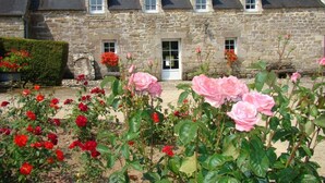 A stone building with multiple windows and a door, surrounded by a garden with red and pink roses.