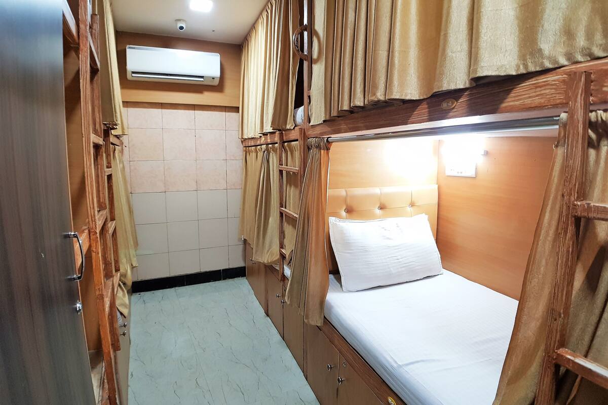 A compact room with a bunk bed, wooden wardrobe, and an air conditioning unit.