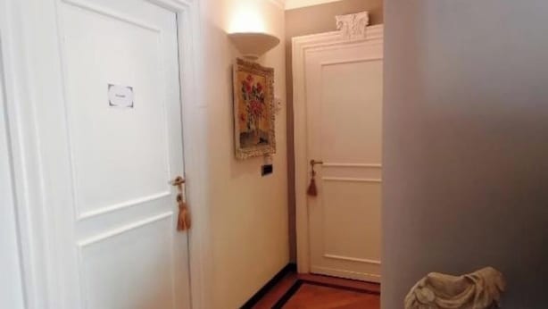Un couloir avec des portes blanches, un plancher en bois et une petite table sur laquelle est posé un vase de fleurs.