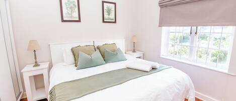 A bedroom with a large bed, two bedside tables, a window with a view, and two framed pictures on the wall.