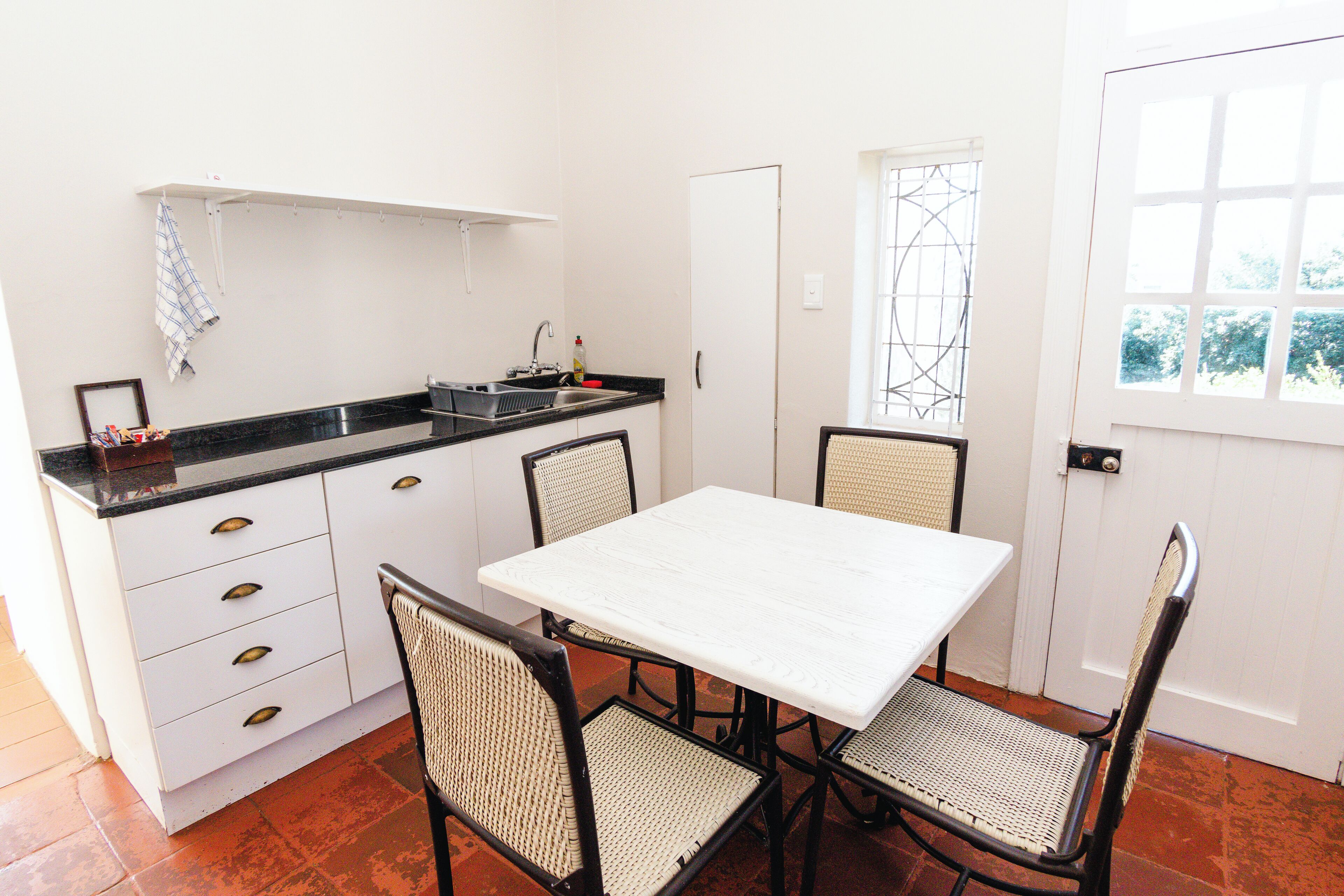 A compact kitchen with white cabinets, a black countertop, and a white table with four chairs.