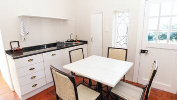 Cozinha compacta com armários brancos, bancada preta e mesa branca com quatro cadeiras.