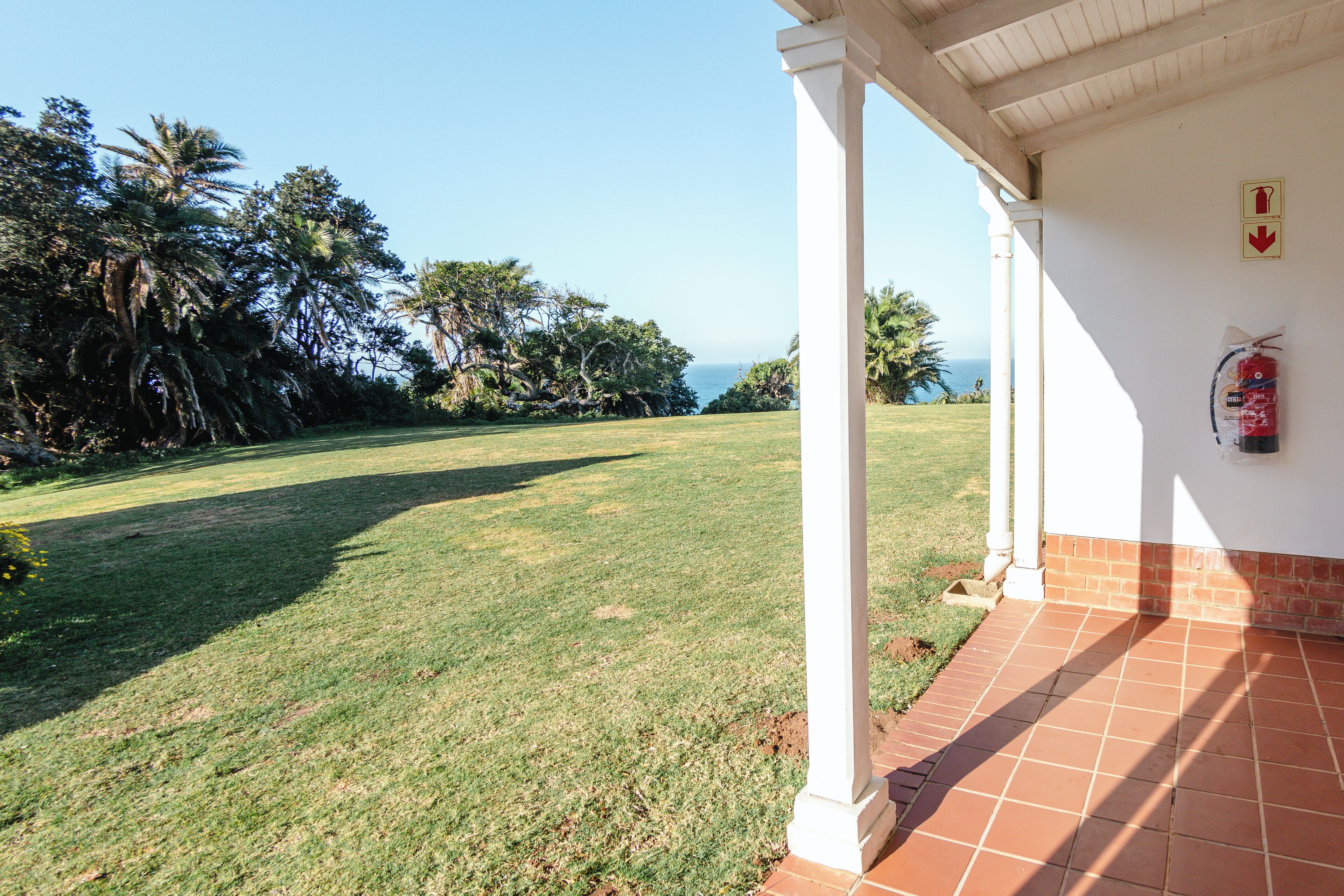 A covered patio with a view of a grassy area and palm trees.