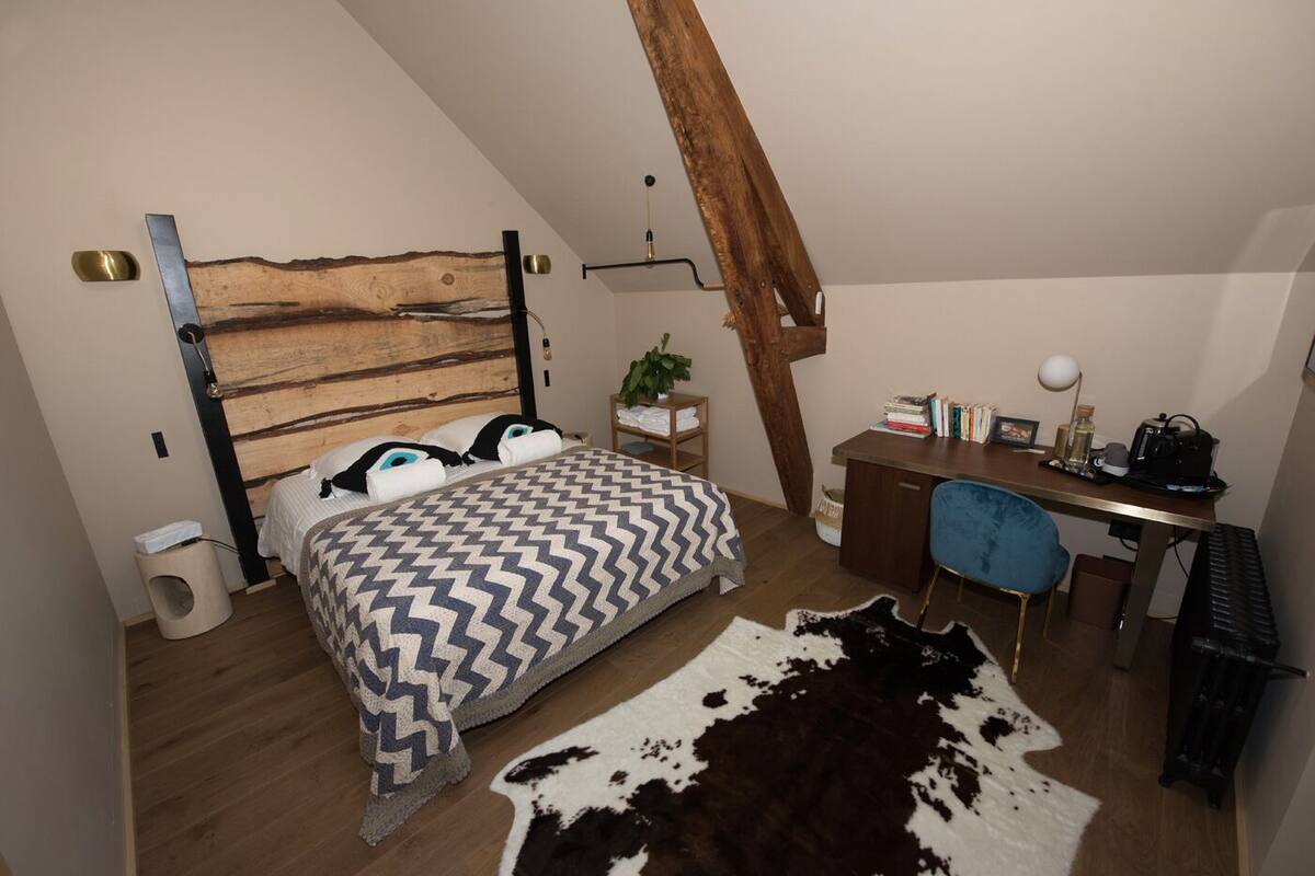 A bedroom with a wooden headboard, a bed with patterned bedding, a desk with a chair, a cowhide rug, and a small plant.