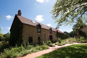 A rustic stone building with a brick roof, surrounded by lush greenery and a paved pathway. - La Barboire Campagne - Chambres (Saint-Laurent-Nouan)