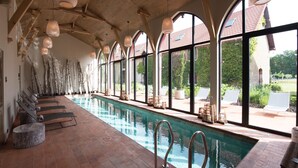 An indoor swimming pool with a long, narrow layout, surrounded by large windows and wooden beams.