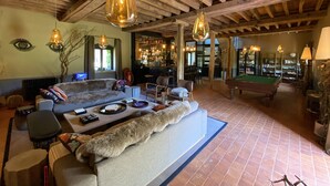 A cozy lounge area with a sofa, chairs, a pool table, and a bar area with shelves and bottles.