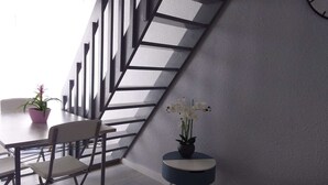 Un interior moderno con una escalera, una mesa de comedor con sillas, una mesita redonda con una planta y un cojín estampado.