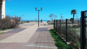 Un camino pavimentado que conduce a una playa, con una cerca a un lado y una palmera al otro.