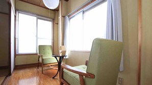 A room with wooden flooring, two green armchairs, a small table, and a white lamp. - Goraku Shinfukae (Osaka)