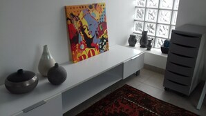 A modern living room with a white console table, decorative vases, a colorful painting, and a window with patterned blinds.