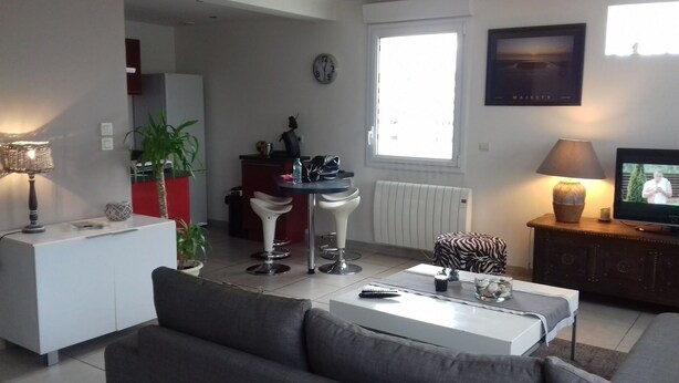 A modern living room with a sofa, a dining table with bar stools, a TV, and a window with a view.