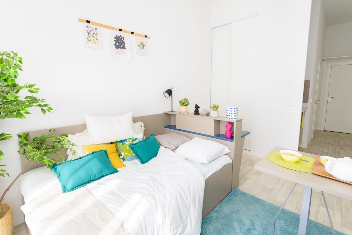 Ein ordentlich eingerichtetes Schlafzimmer mit einem Bett, Nachttisch und einem kleinen Tisch mit Schüssel und Tellern.