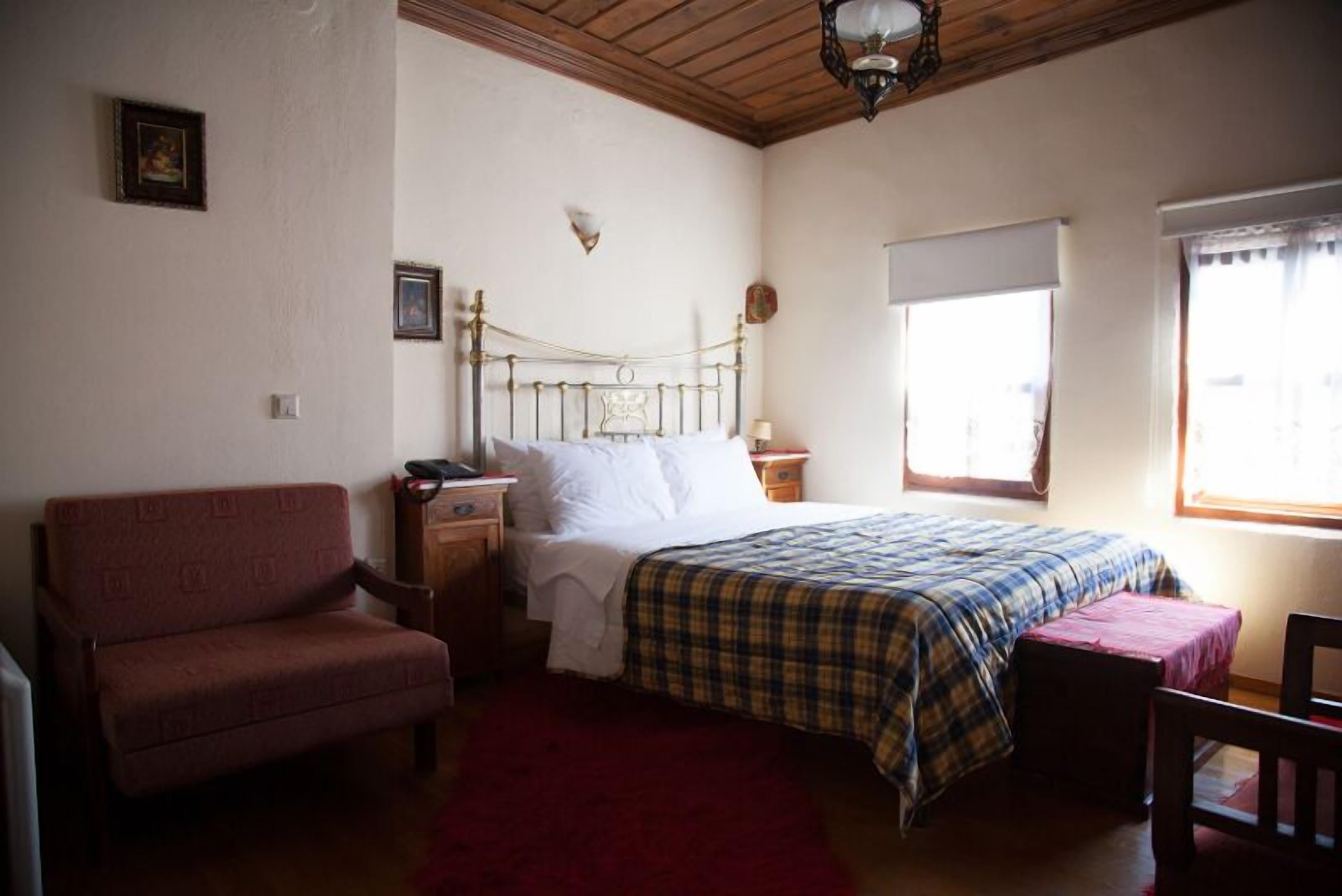 Un dormitorio con una cama, una silla, una mesita de noche, un ventanal y una lámpara en el techo.