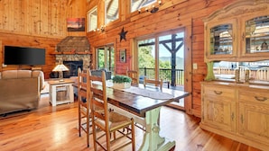L’intérieur d’un chalet en bois comprend une table à manger, des chaises, une cheminée, un téléviseur et un coin cuisine.