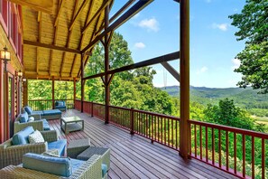 A covered outdoor deck with wicker furniture and a red railing, overlooking a lush landscape.